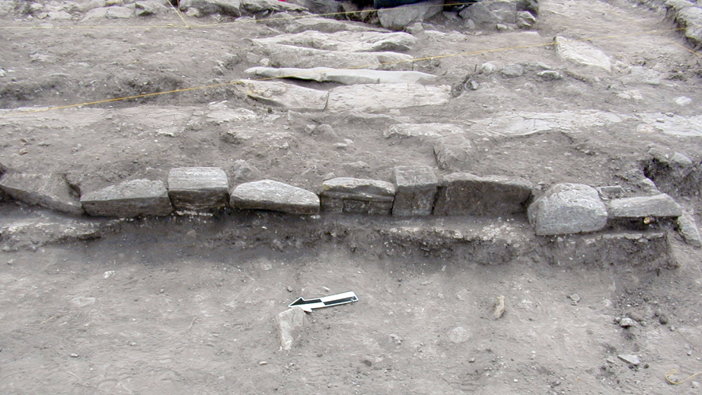The image foreground is the surface of a domestic patio with small remnants of white plaster, while the tomb was situated under a room of the house (positioned on the terrace)